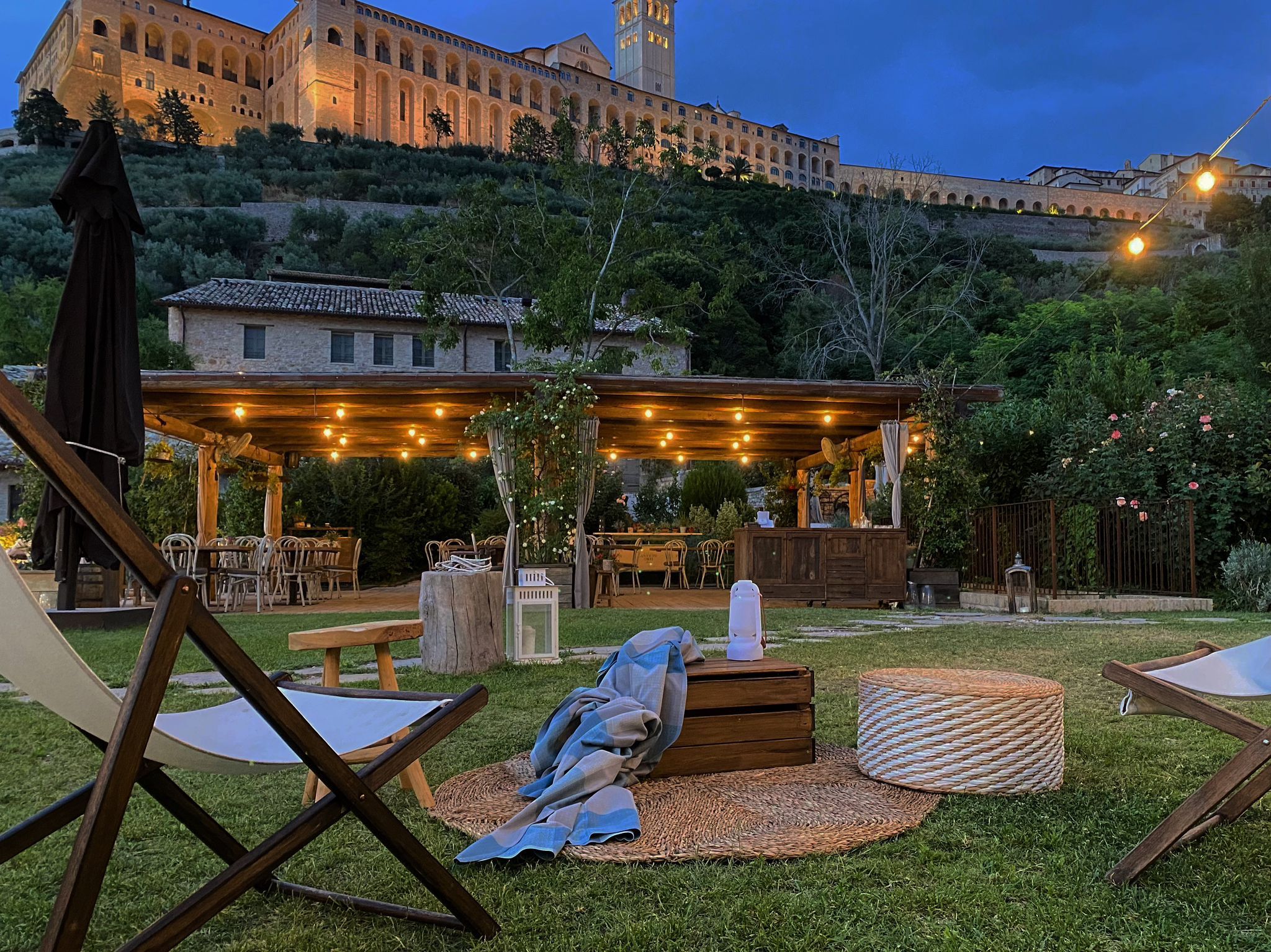 A medieval hamlet at evening, the illuminated Basilica above the gardens