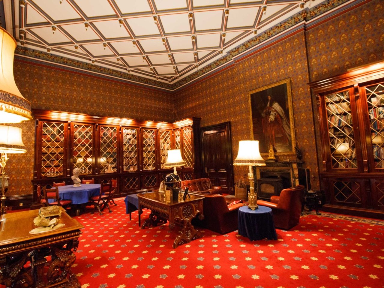 A panelled room with a coffered ceiling, portraits and a red carpet