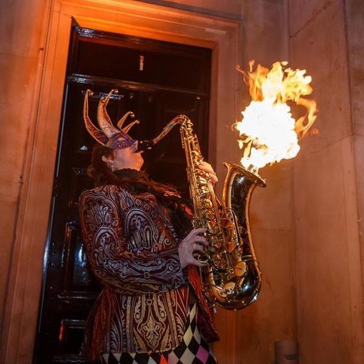 A costumed performer playing a flaming saxophone in a panelled doorway