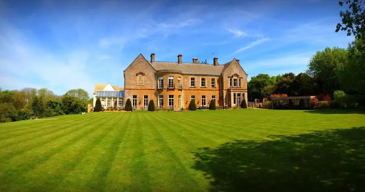 The honey Cotswold-stone Georgian manor across frosted lawns, its orangery wing