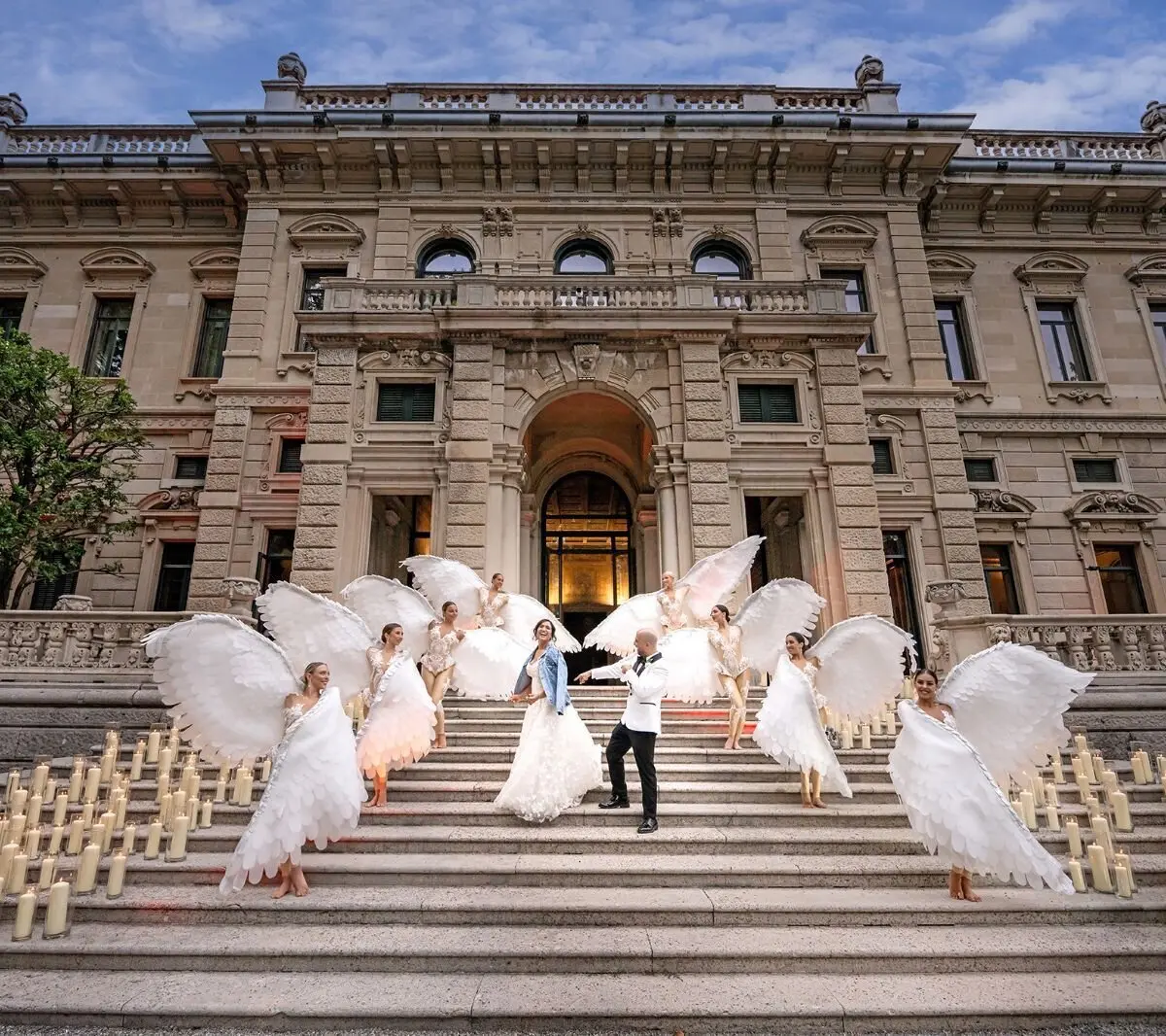A bride and groom welcomed onto a candlelit stone staircase by performers in feathered wing costumes