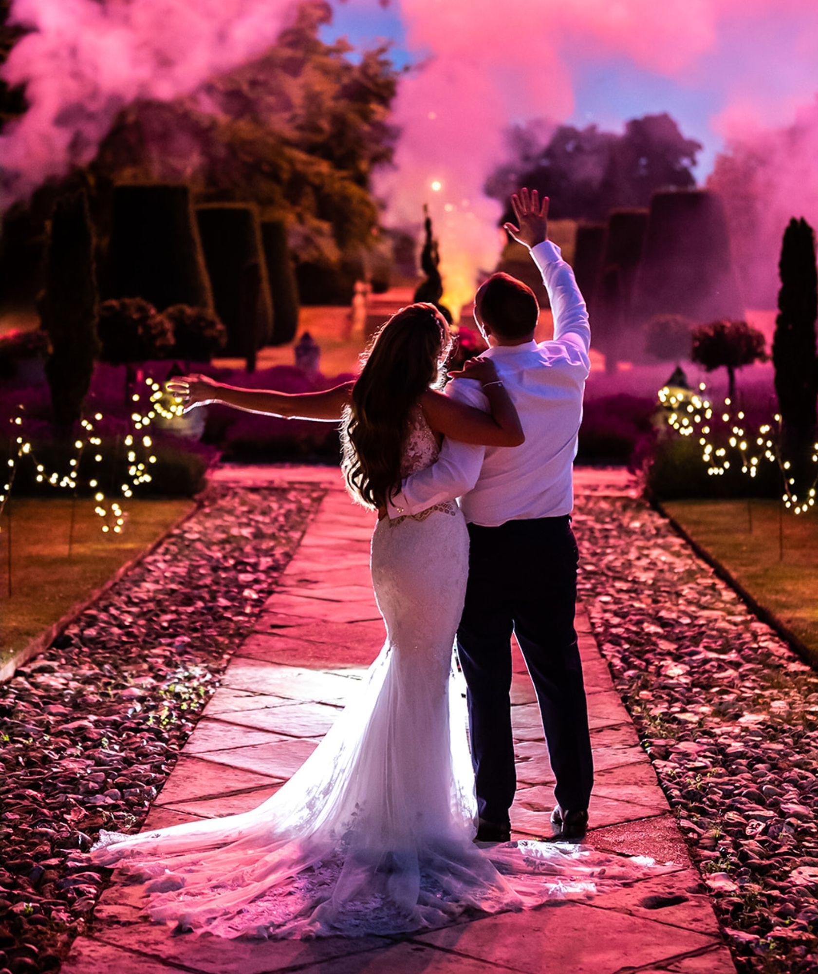 A couple at dusk on a petal-strewn path, lit by rose-coloured smoke