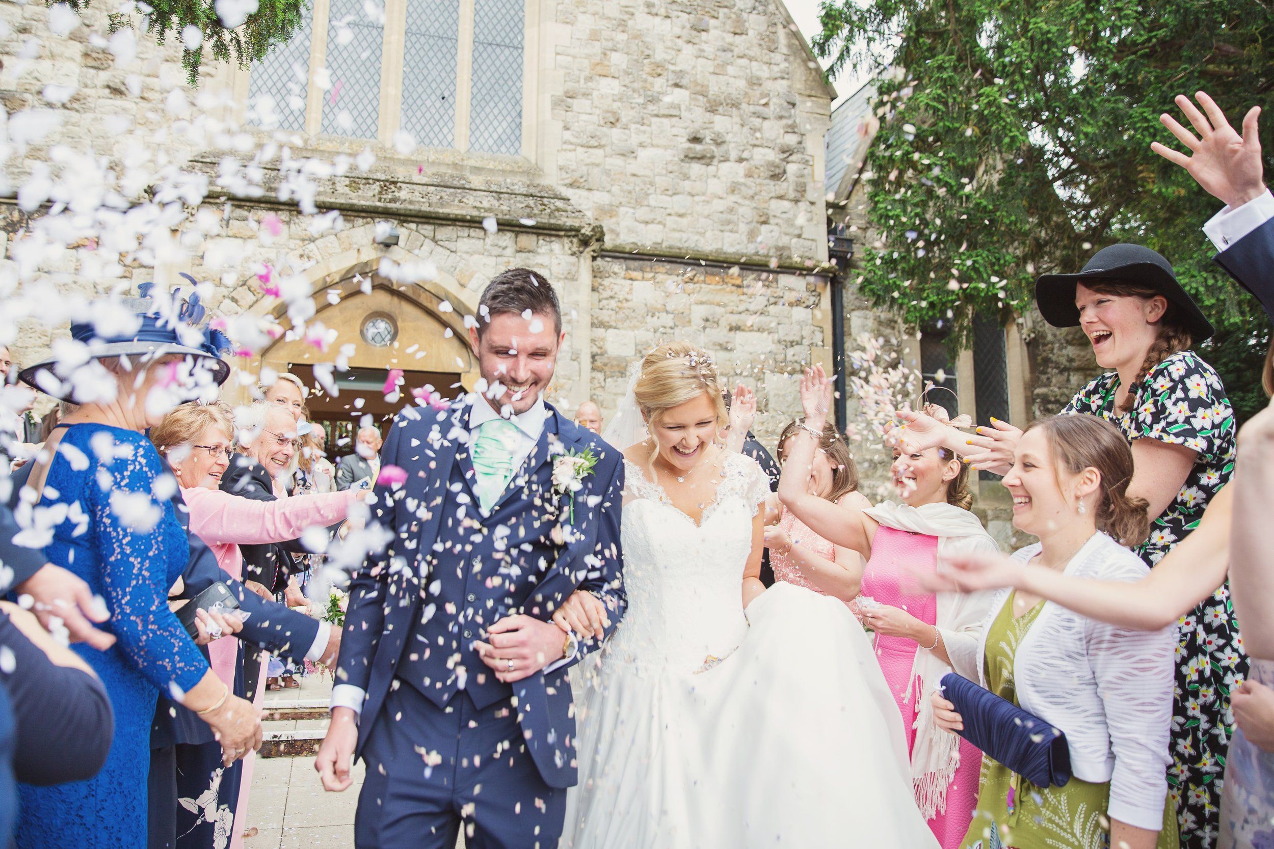 A bride and groom walking through confetti outside a stone church