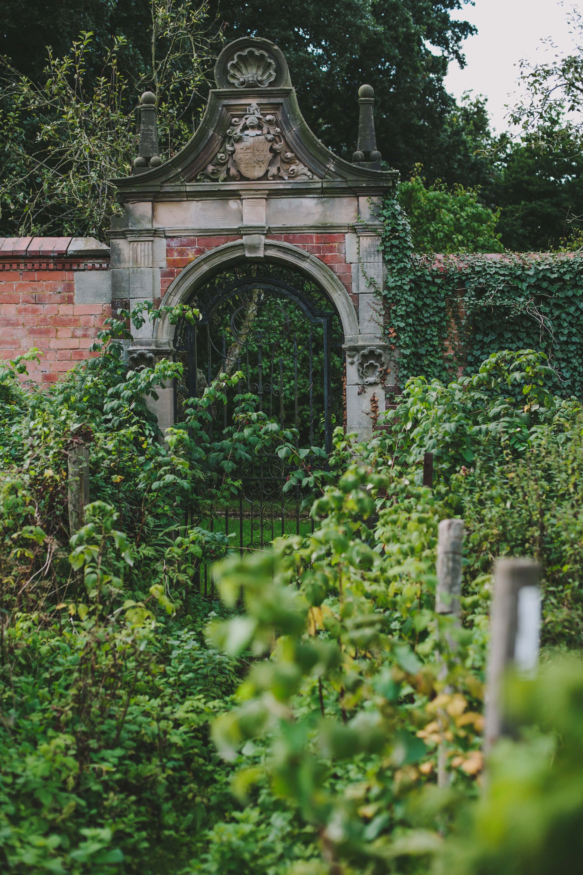 A weathered brick archway leading into the Victorian walled garden, thick with greenery, Hampton Manor, Hampton-in-Arden, England