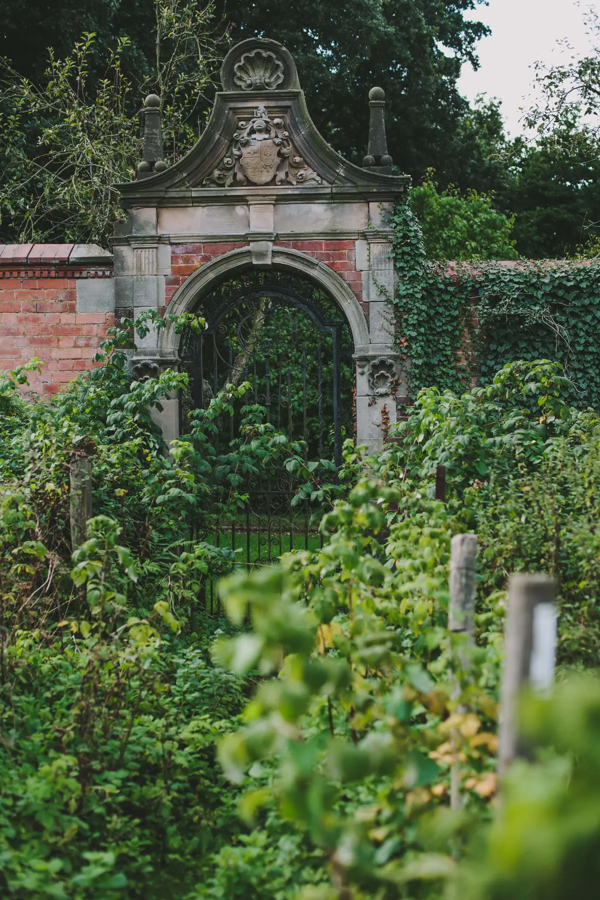 A weathered brick archway leading into the Victorian walled garden, thick with greenery, Hampton Manor, Hampton-in-Arden, England