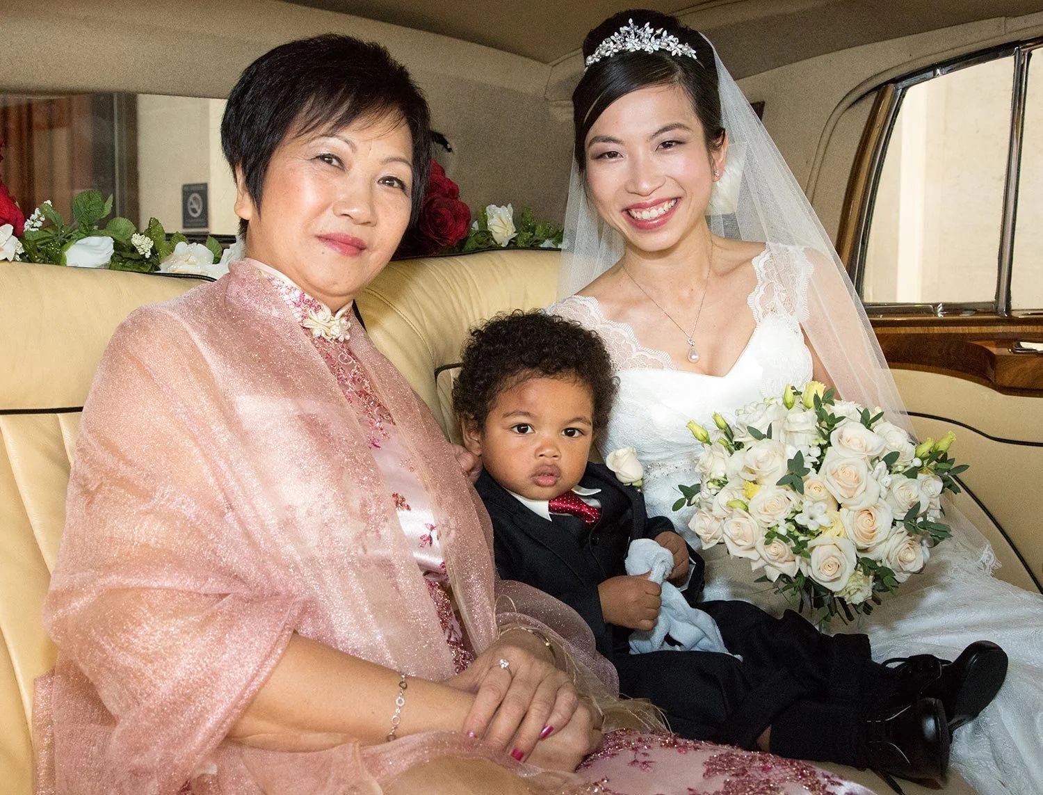 A bride with her mother and a young pageboy in the wedding car