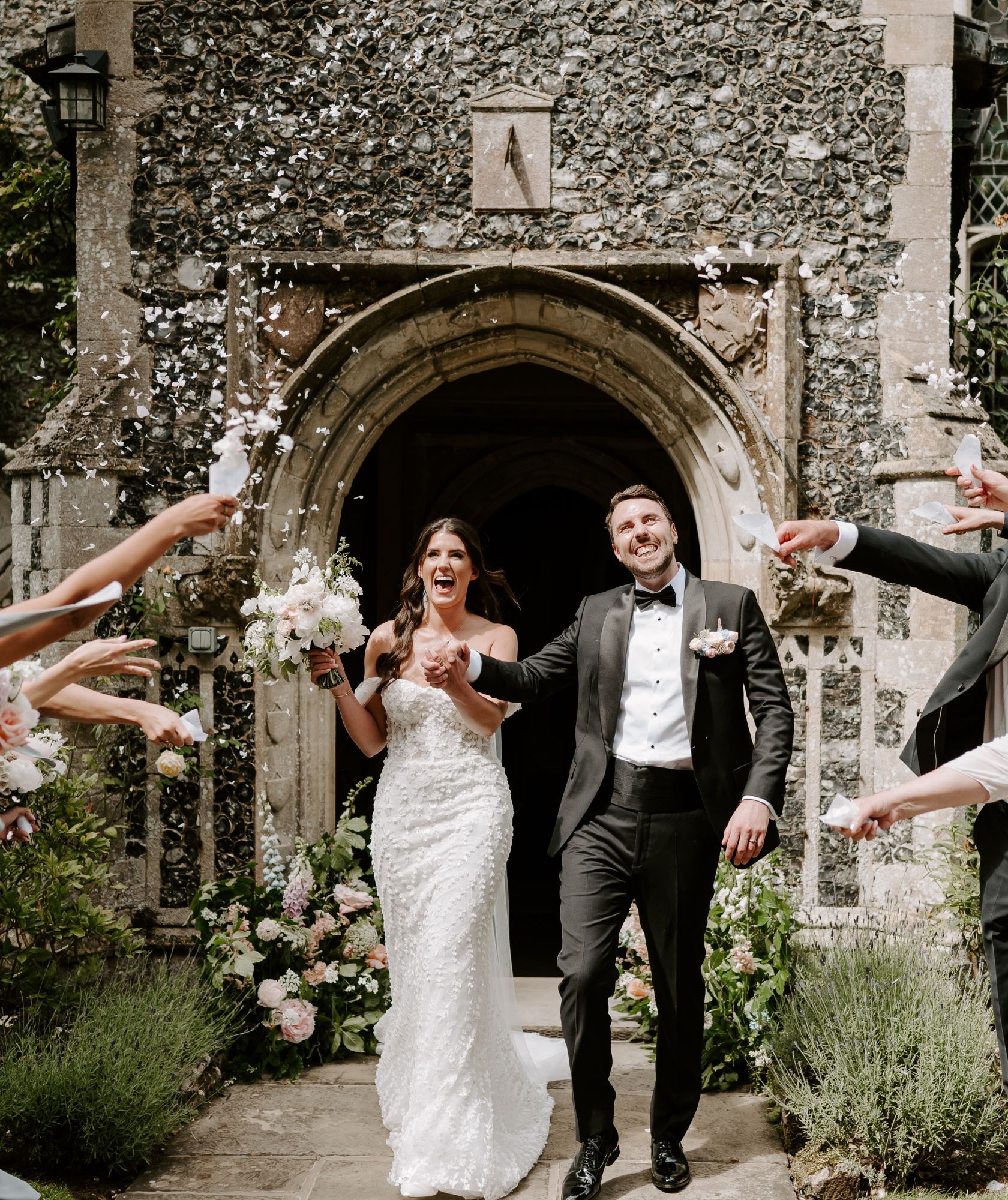 A couple step through the Gothic stone archway of the house in a shower of confetti