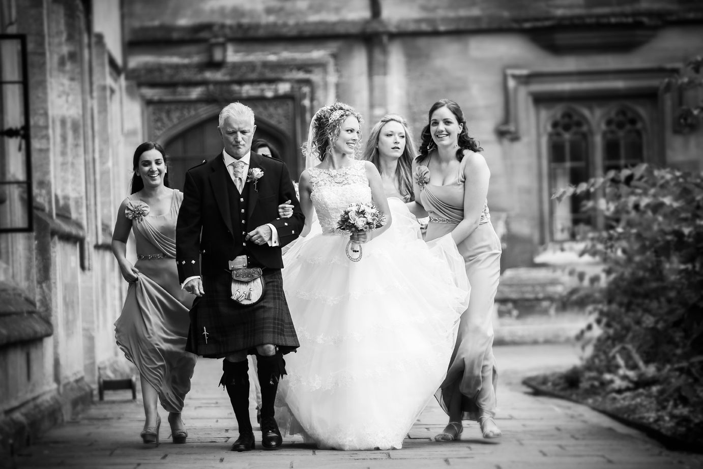 A bride walking in with her father and two bridesmaids, stone archway behind them, Nadine Pyke Make Up Artist, Surrey, England