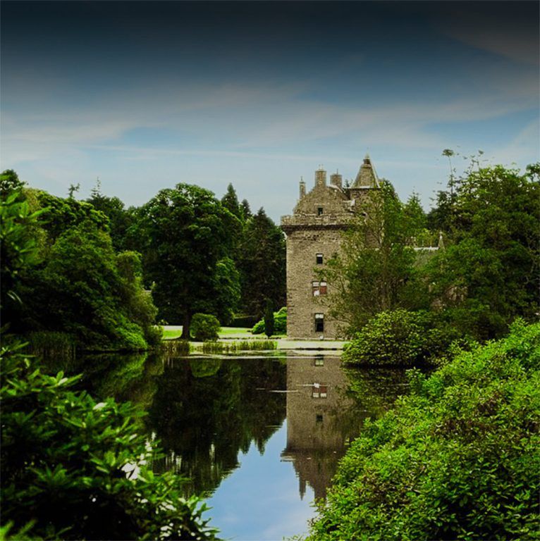 The castle tower mirrored in the still loch, backed by deep green woods