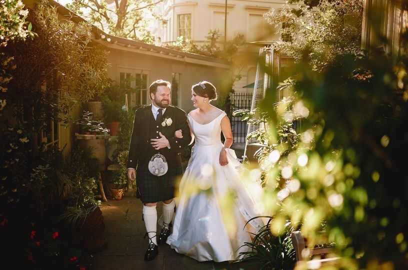 The bride and groom walking through the greenery-lined garden terrace at golden hour