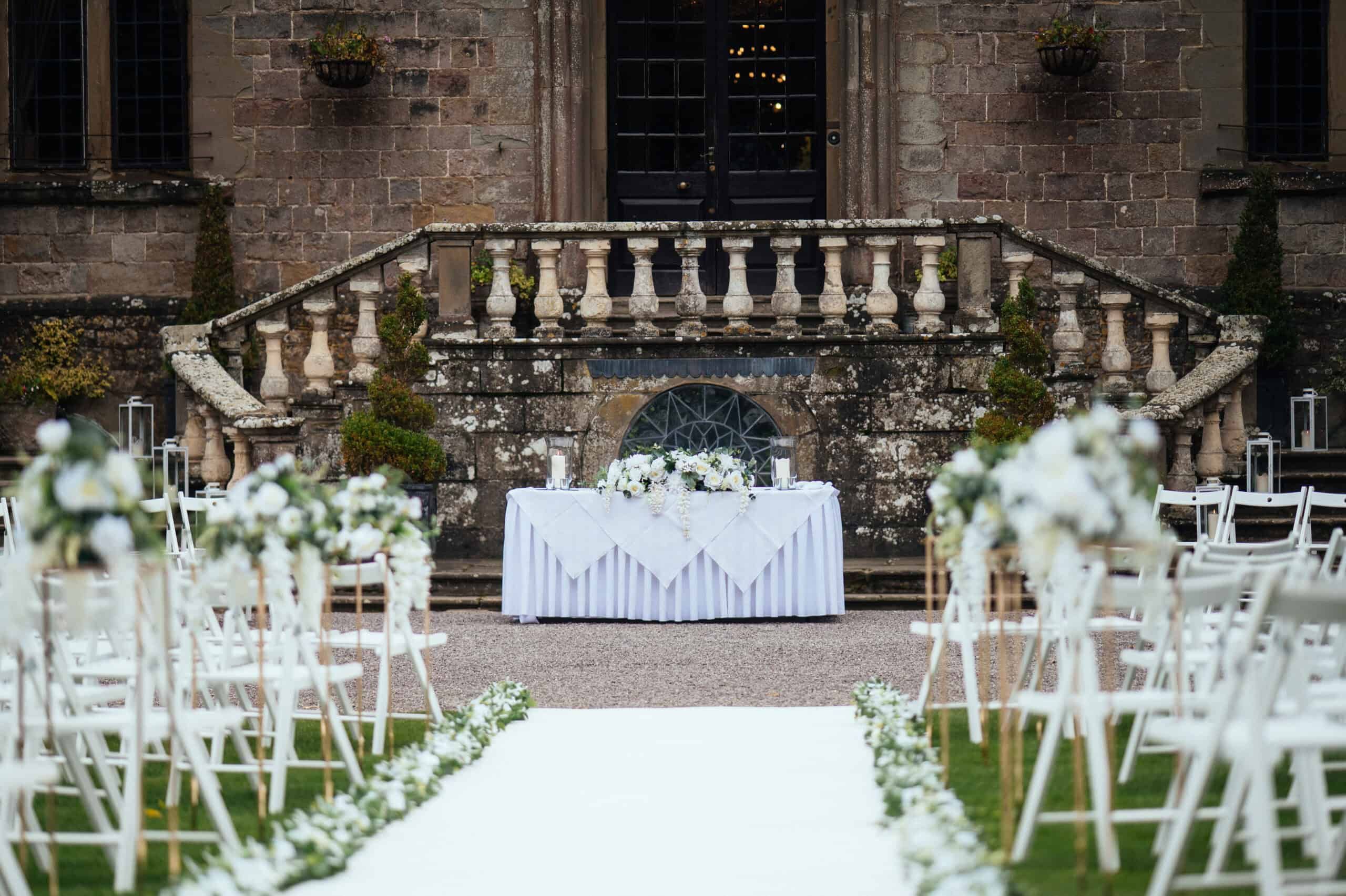 An outdoor ceremony on the terrace, the balustraded steps and registrar's table dressed with white florals, Clearwell Castle, Clearwell, England