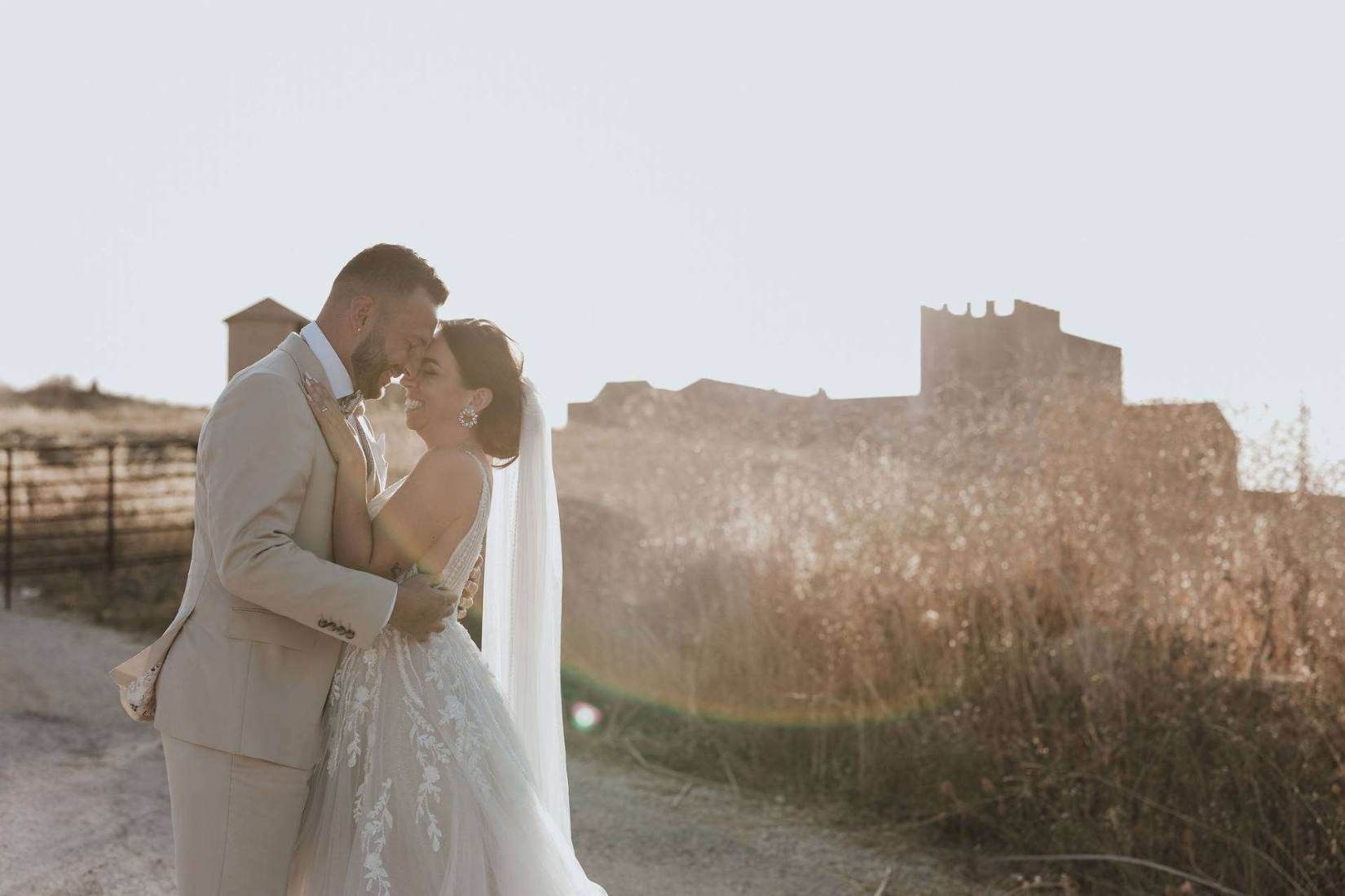 A bride and groom embracing at golden hour, a fortified stone farmhouse compound behind them