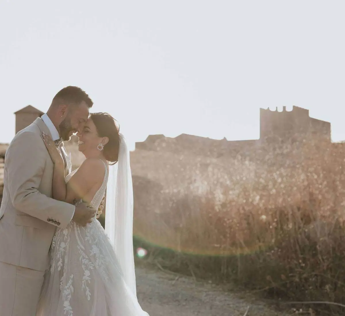 A bride and groom embracing at golden hour, a fortified stone farmhouse compound behind them