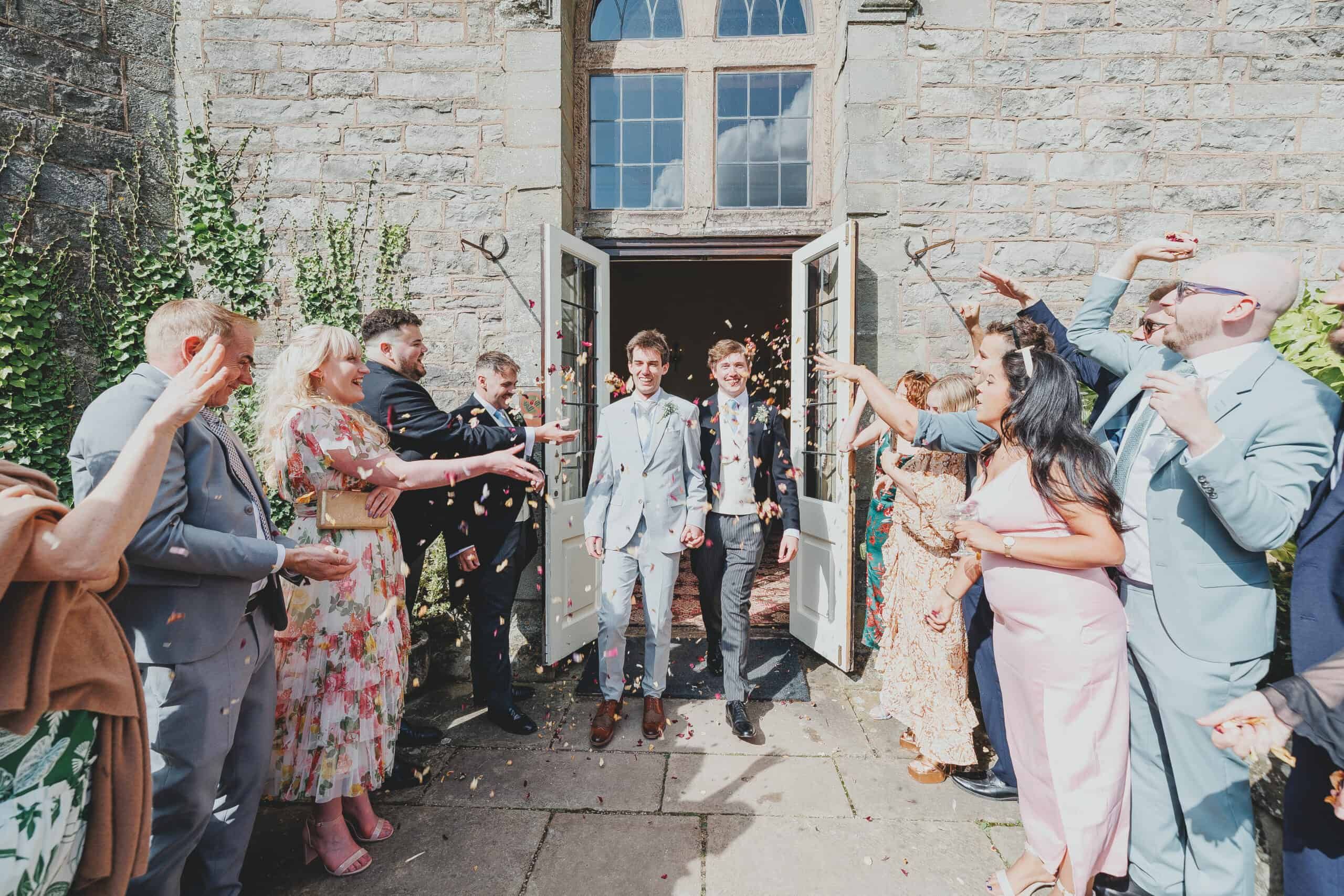 A confetti send-off, the couple stepping from the castle doorway through a shower thrown by guests