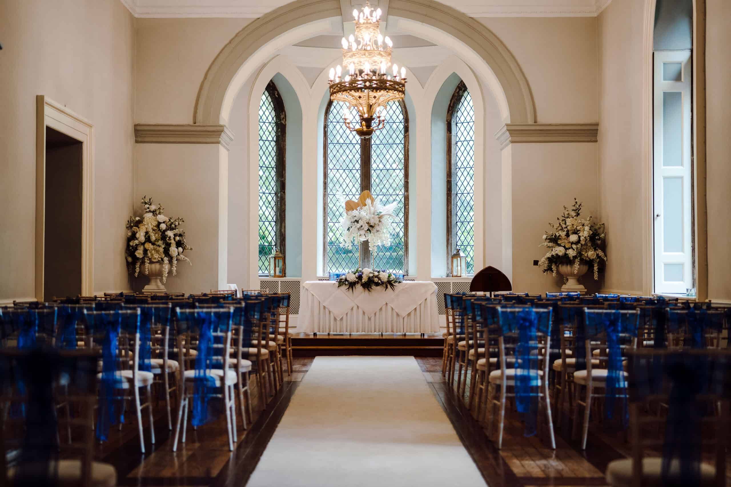 A Ballroom ceremony with blue sashes, the registrar's table below the arched leaded window and chandelier