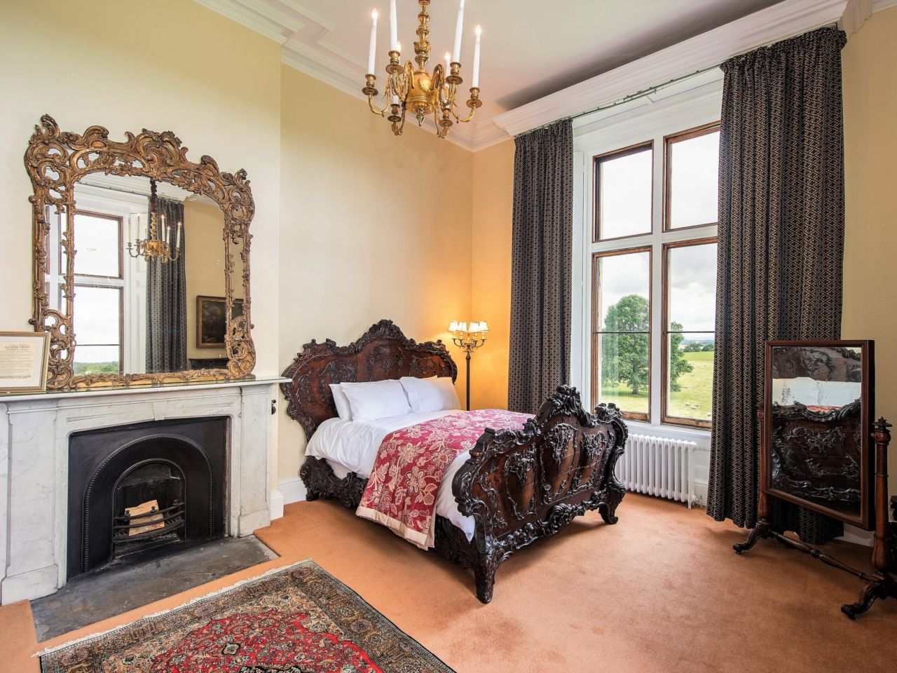 A bedroom with a carved bed, marble fireplace and gilt mirror
