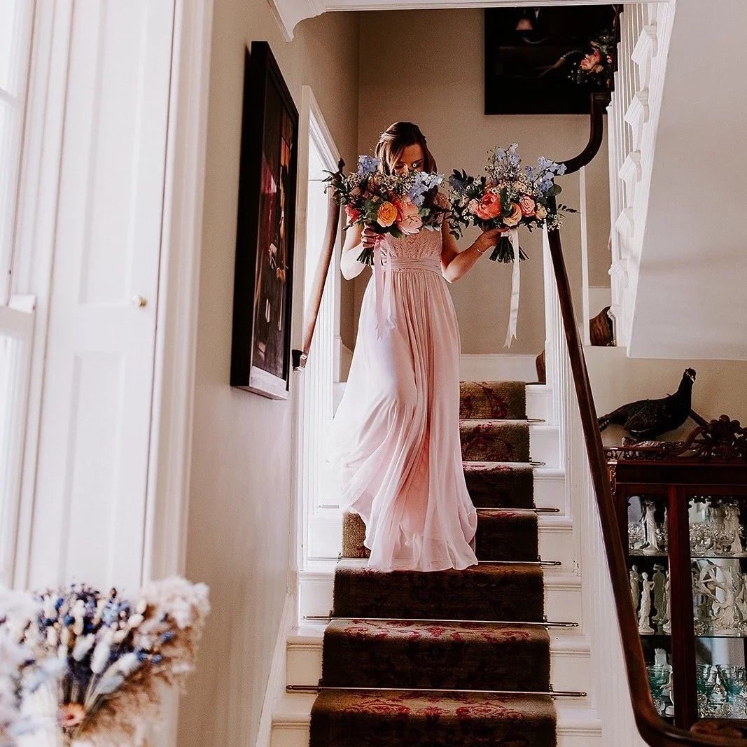 Carrying matching bouquets down a country house staircase