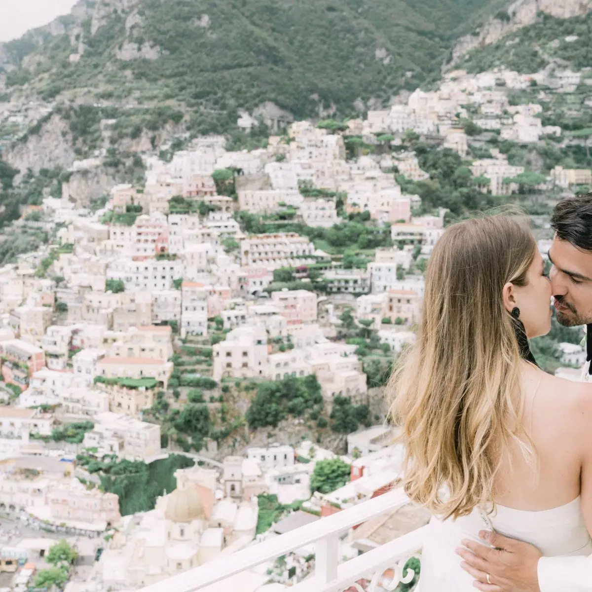 A couple kissing on a balcony above Positano, the pastel town stacked below