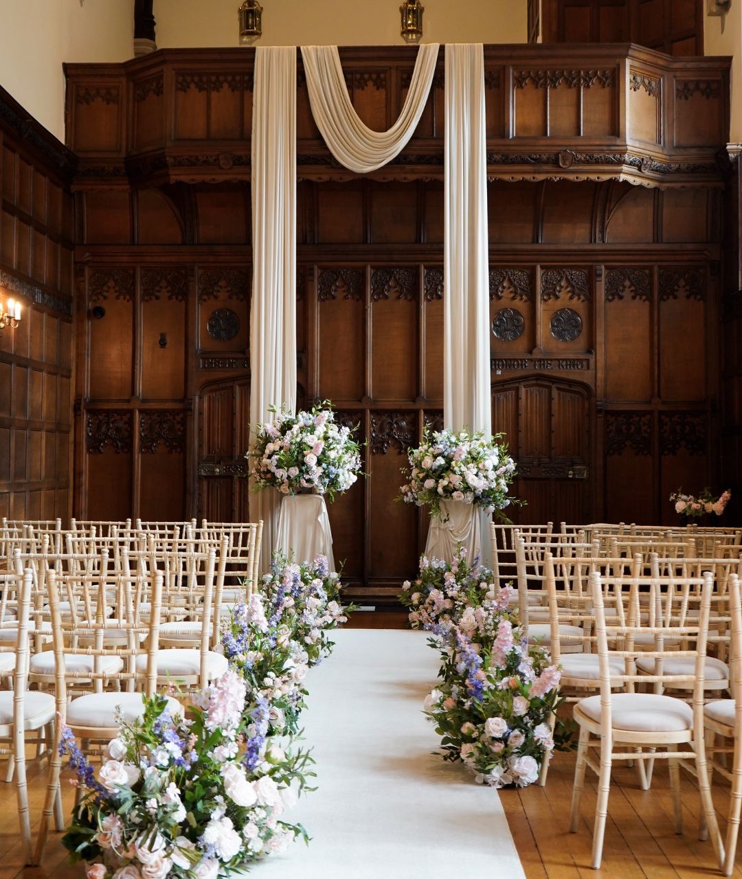 A ceremony set in the panelled Banqueting Hall, chairs arranged before floral-draped columns