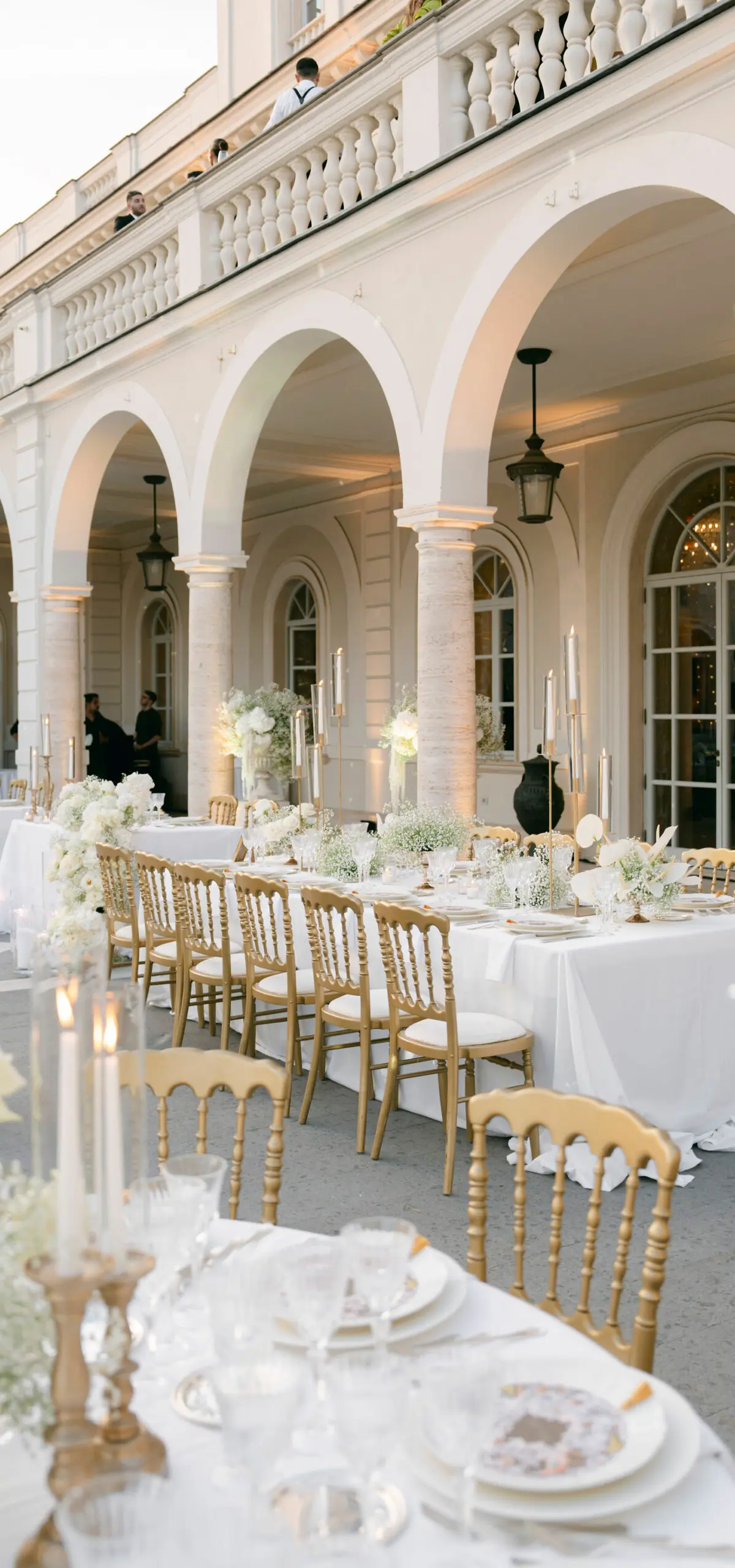 A long table under the arcade of a villa loggia, gilt chairs the length of it