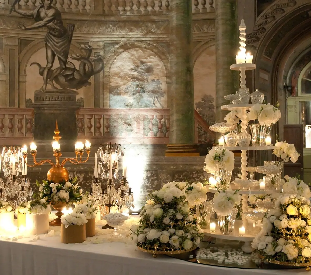 A tower of white sweets and banks of roses in a painted hall