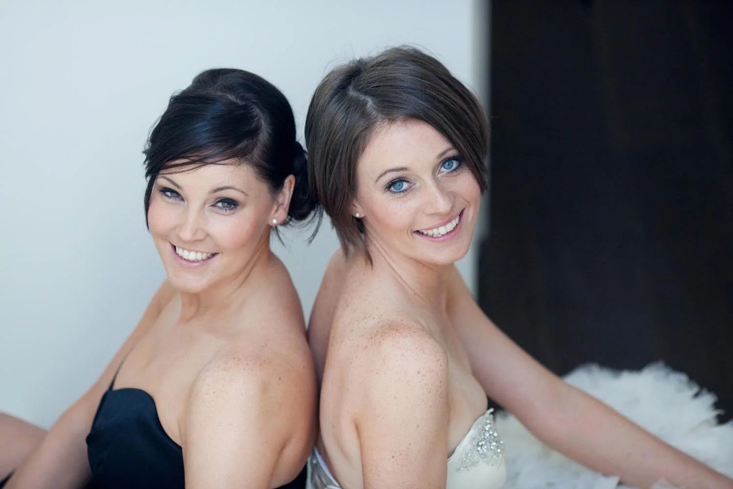 A bride and her chief bridesmaid, matching soft updos, back to back