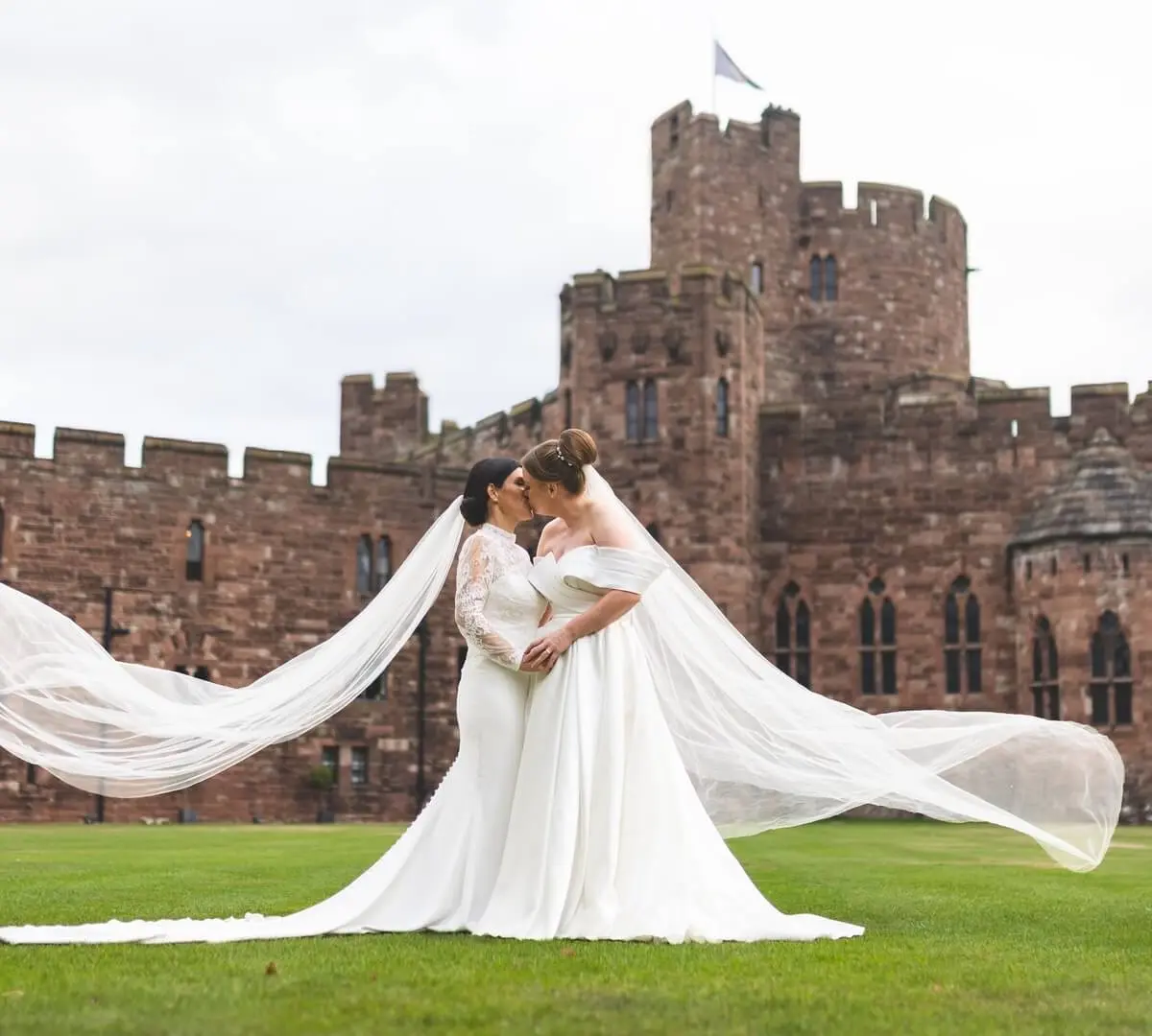 Two brides on the lawn, veils sweeping, the castle behind