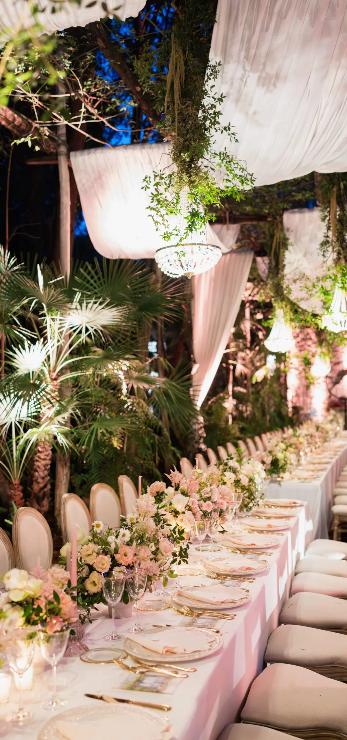A long wedding table under pink drapery and chandeliers