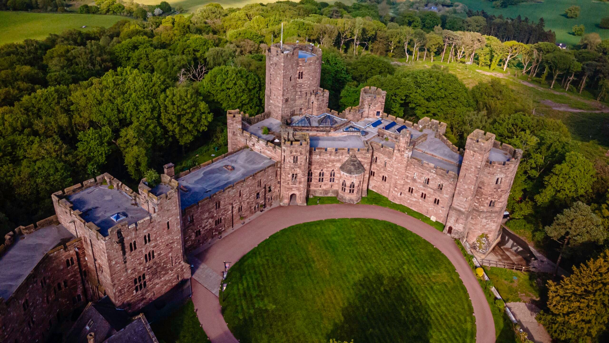 The castle from above, its inner courtyard and circular lawn ringed by towers and battlements, Peckforton Castle, Tarporley, England