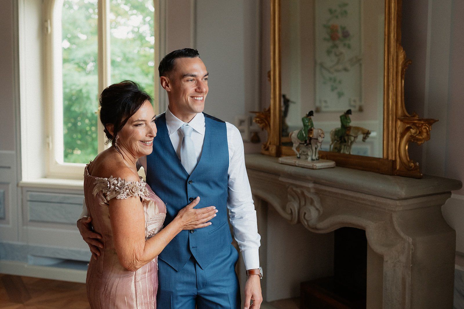 A candid embrace between a groom and his mother beside an antique gilt mirror