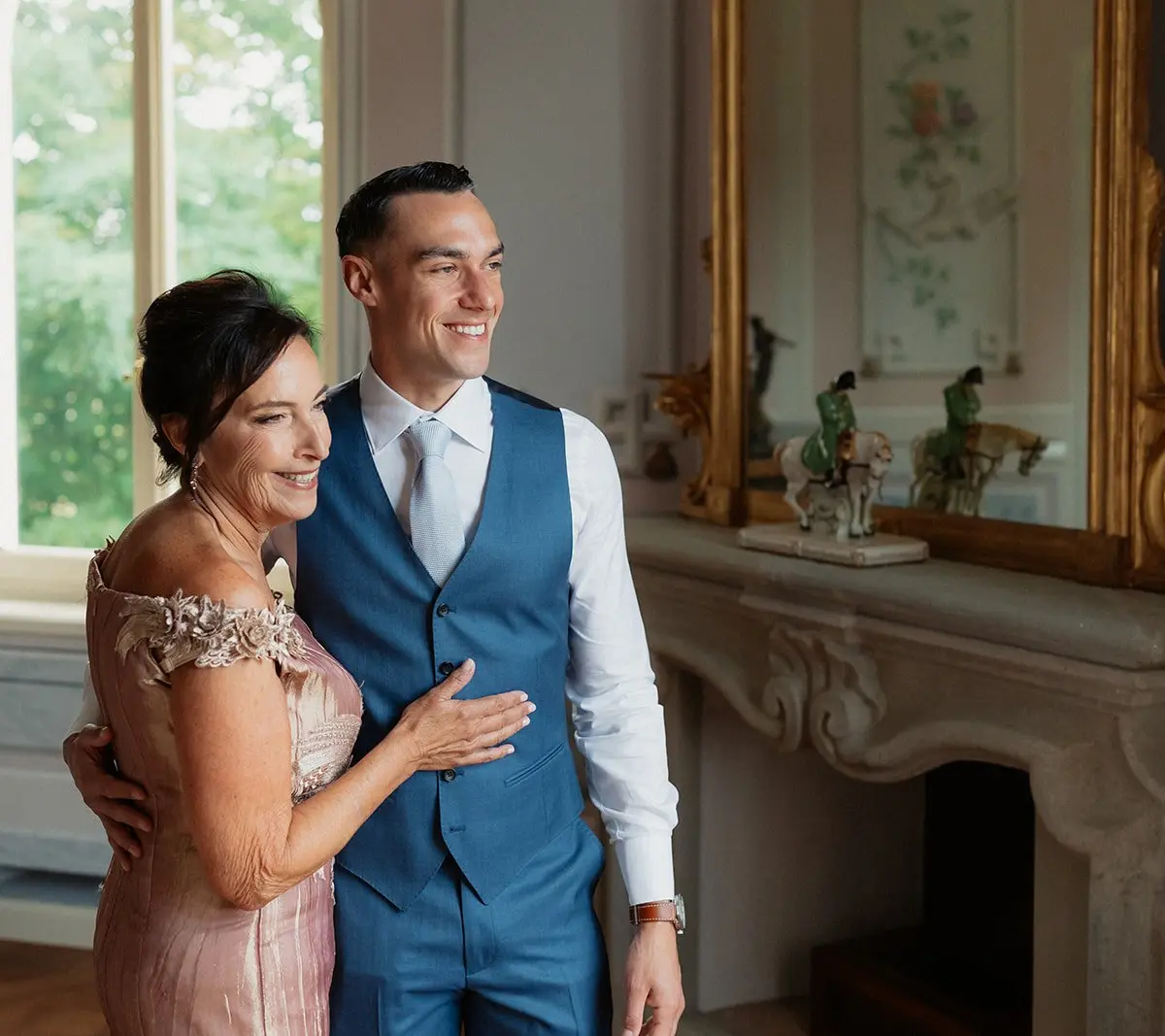 A groom with his arm around his mother beside an antique mirror at Villa Valentini Bonaparte