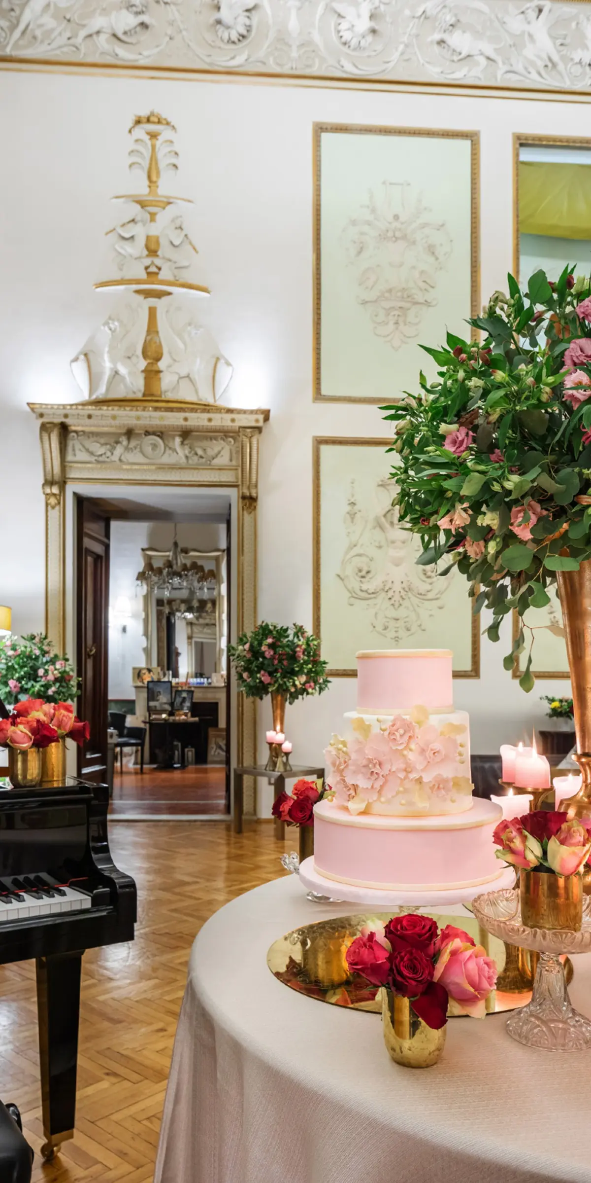 A pale pink wedding cake beside a grand piano in a white and gold Florentine salon