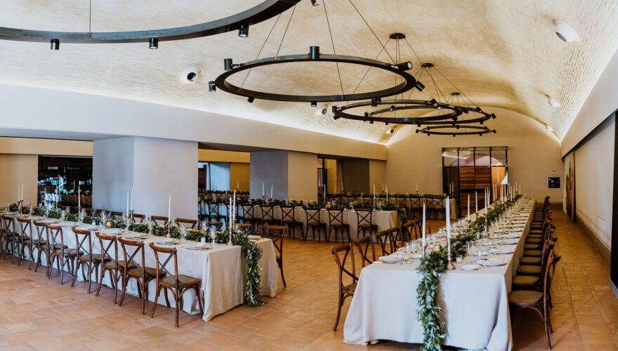 The vaulted stone dining hall, long tables dressed with greenery garlands