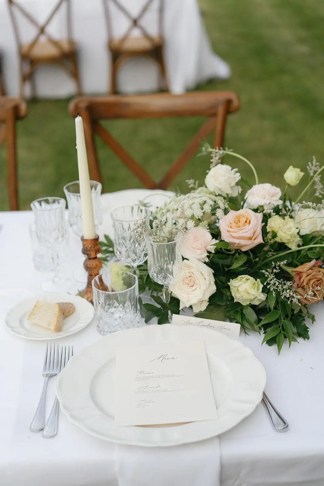 A place setting on the lawn with a menu card, taper candle and garden roses