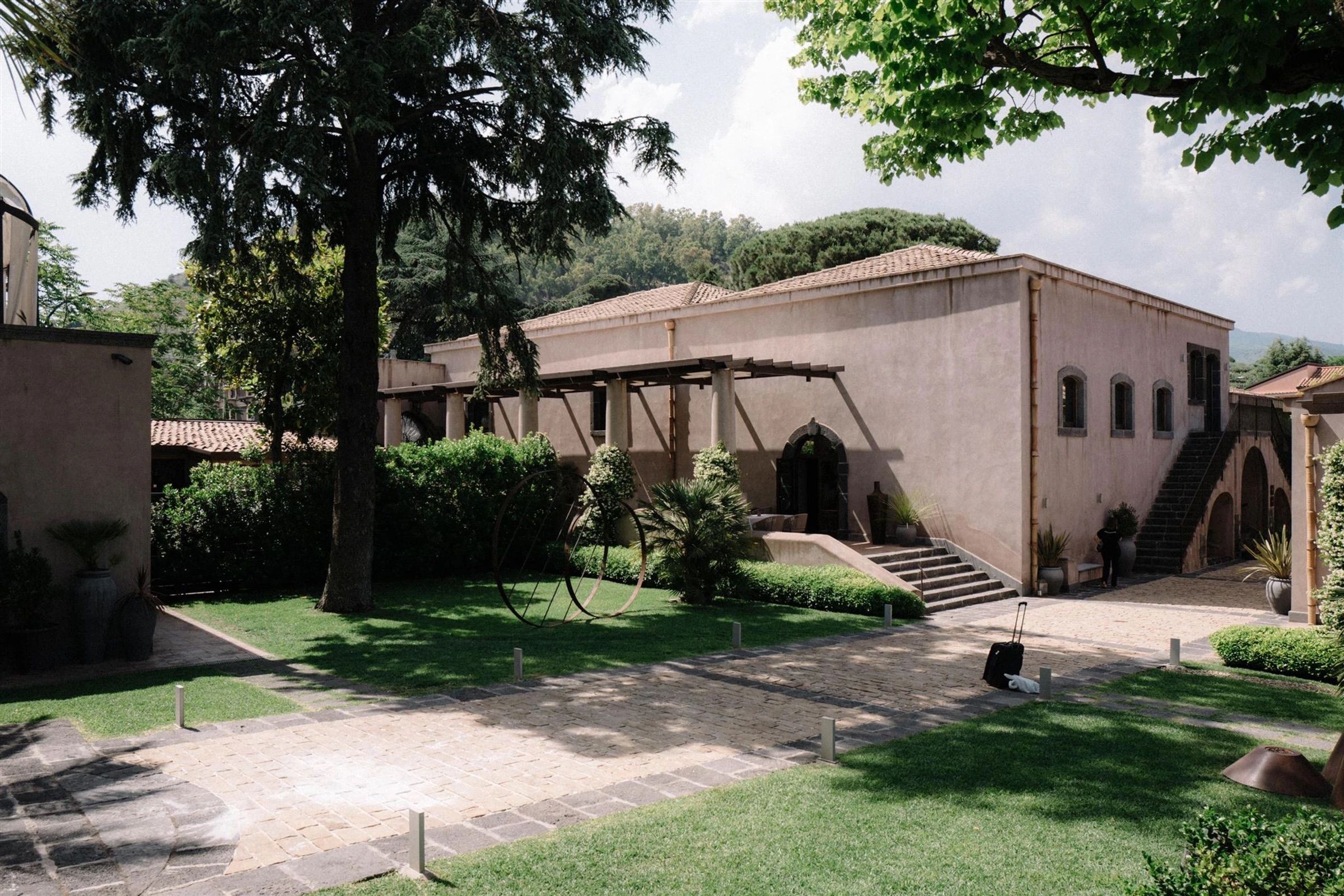 The venue's stone facade and tiled roof, reached along a cobbled drive beneath a wooden pergola and cypress trees