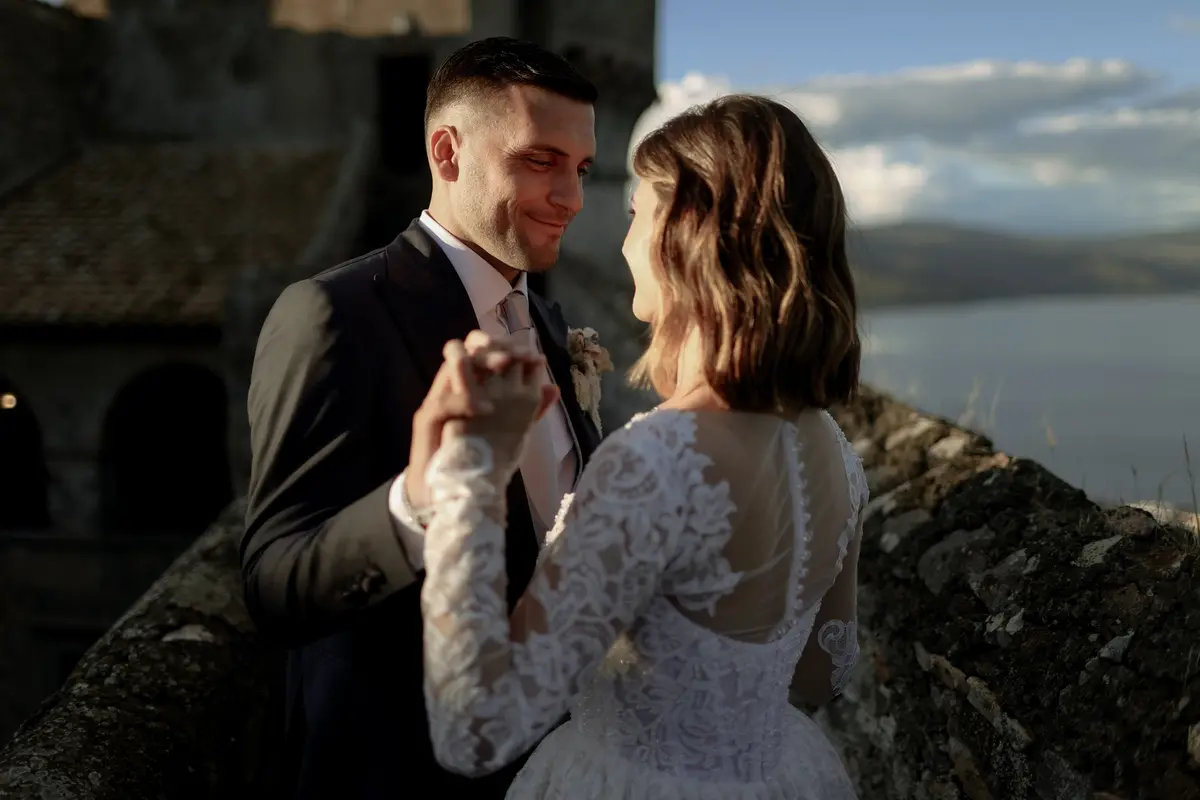 A couple dancing at golden hour beside a stone tower and a still lake