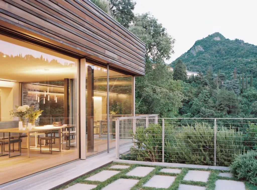 Villa Nascosta at dusk, the lit interior glowing behind the glass above Lake Como, Villa Nascosta, Varenna, Italy