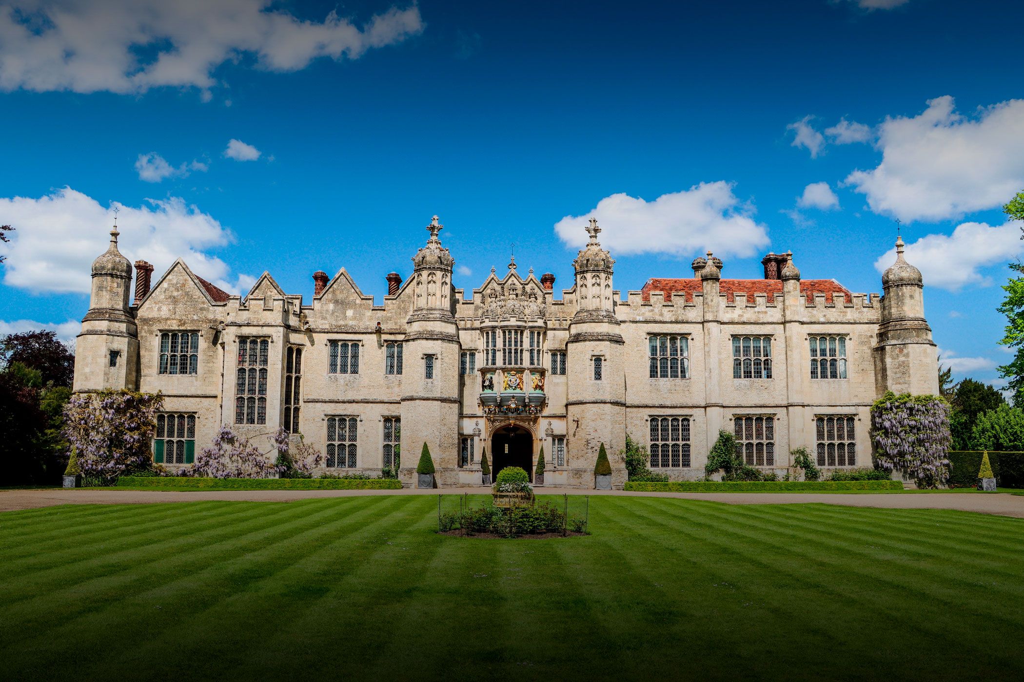The mullioned Tudor facade of Hengrave Hall across a striped lawn under a blue sky