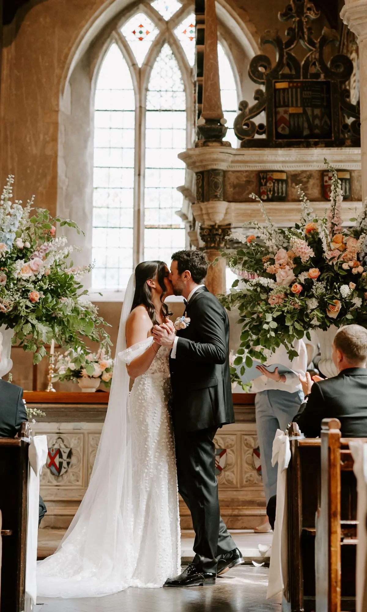 A couple kiss at the altar of the church beneath a Gothic window