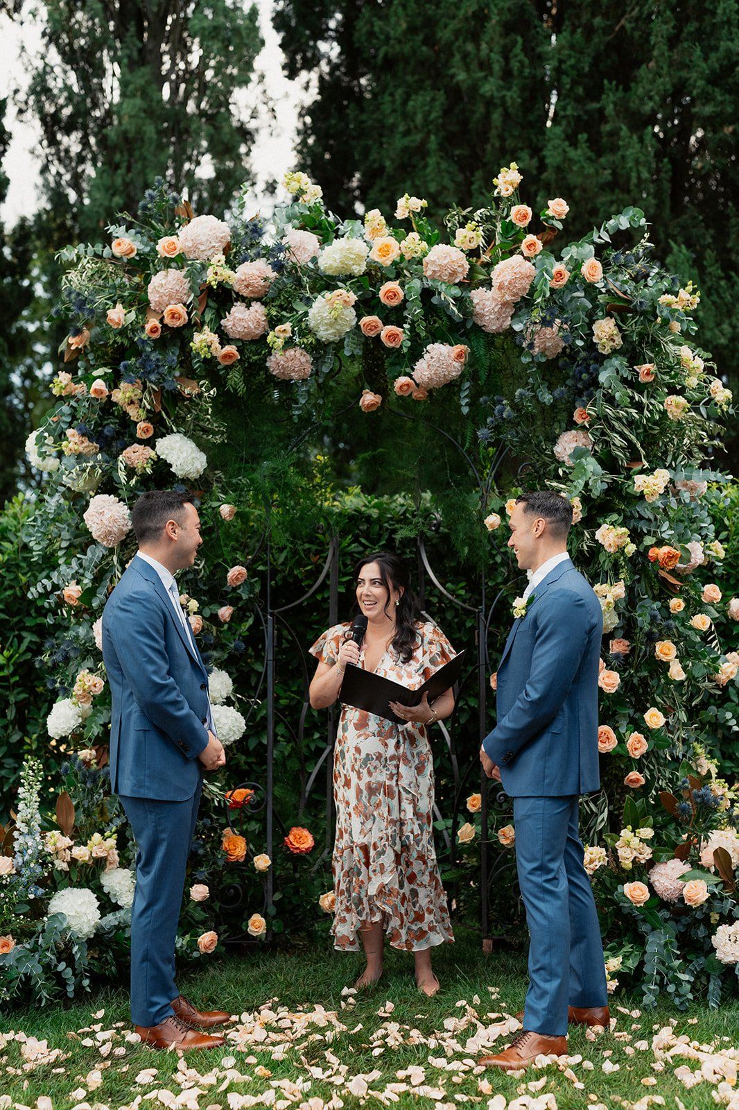 A ceremony under a rose and thistle arch in a Tuscan garden, guests laughing, confetti on the grass