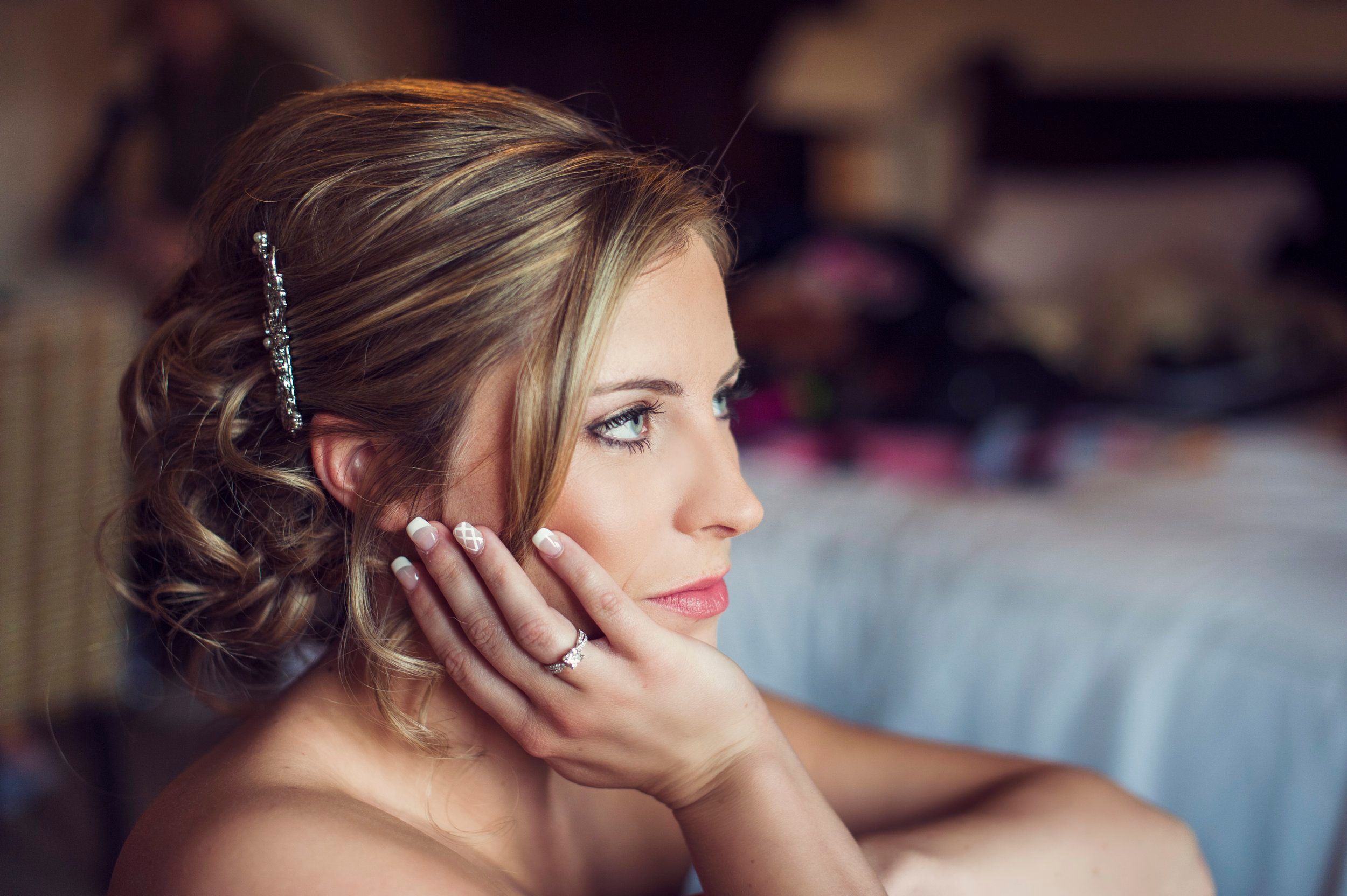 A bride resting her chin on her hand, soft upswept hair