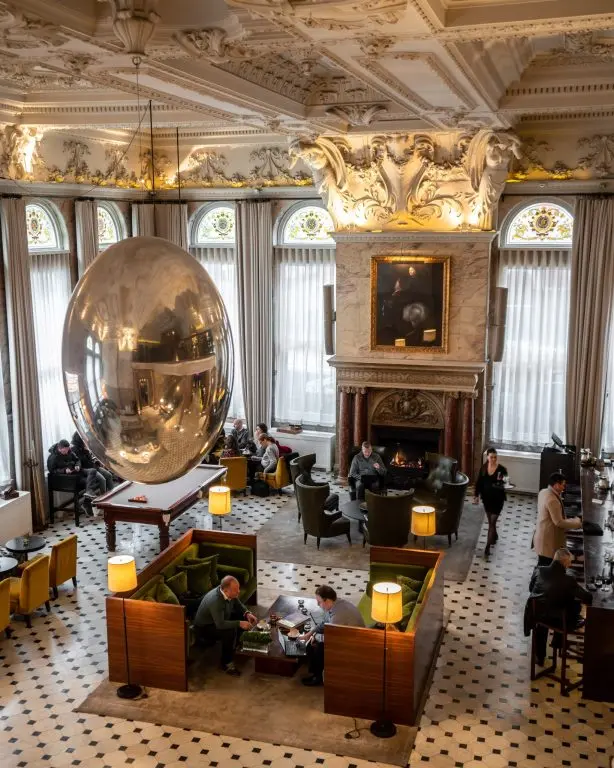 The sculptural lobby lounge, chequerboard floor beneath a silver egg sculpture, fireplace and low seating, The London EDITION, London, England