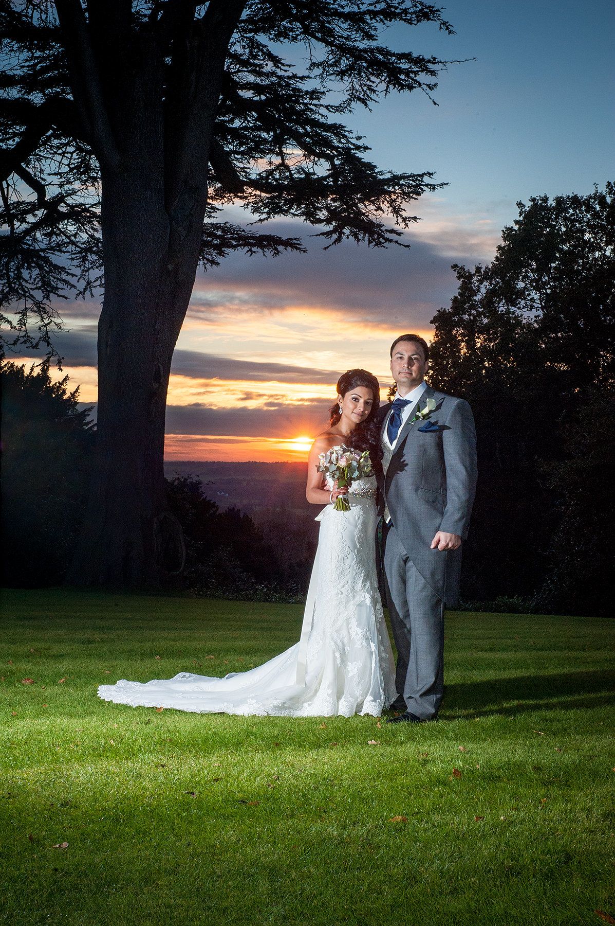 A bride and groom in a grassy field at sunset