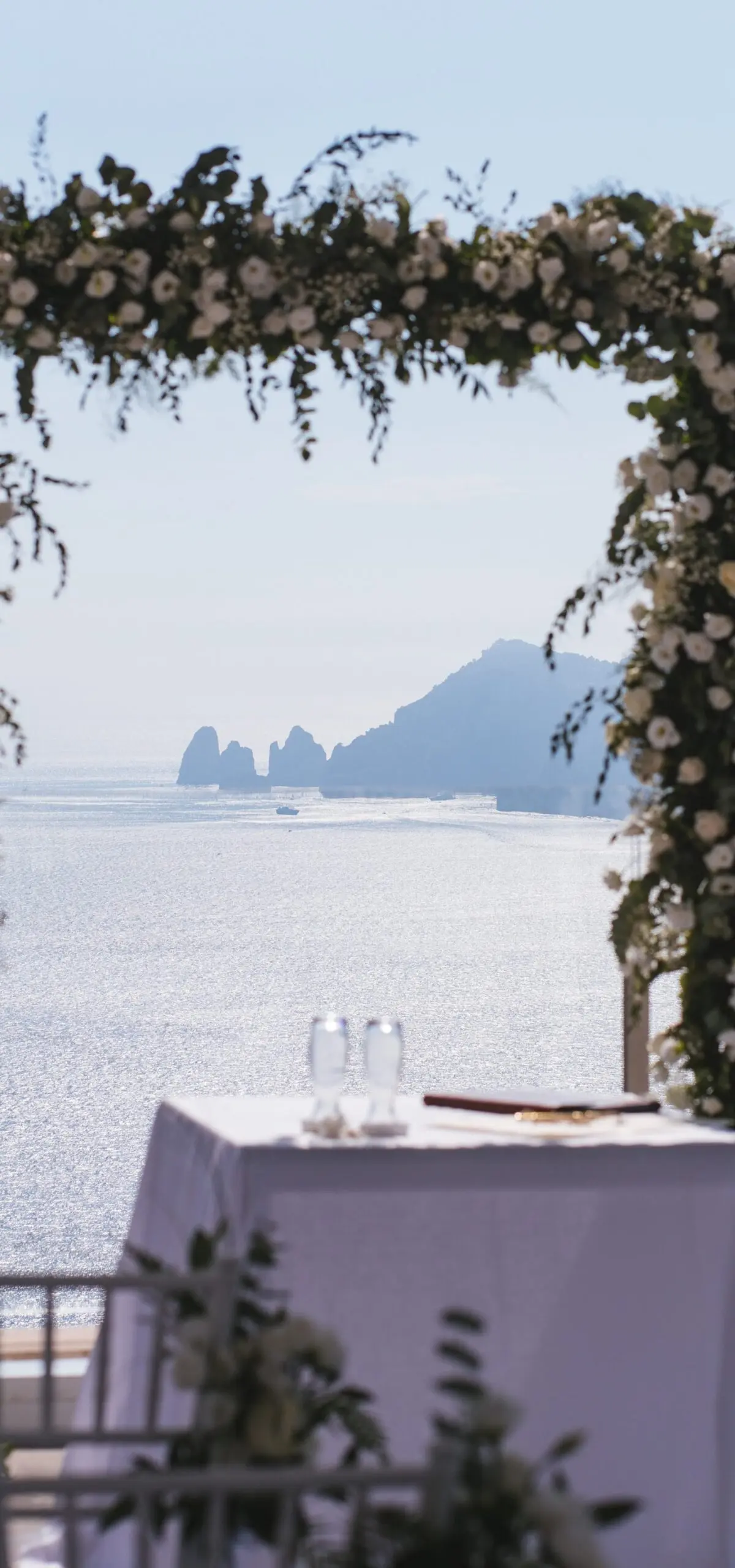 A floral arch framing the Faraglioni rock stacks of Capri across the water