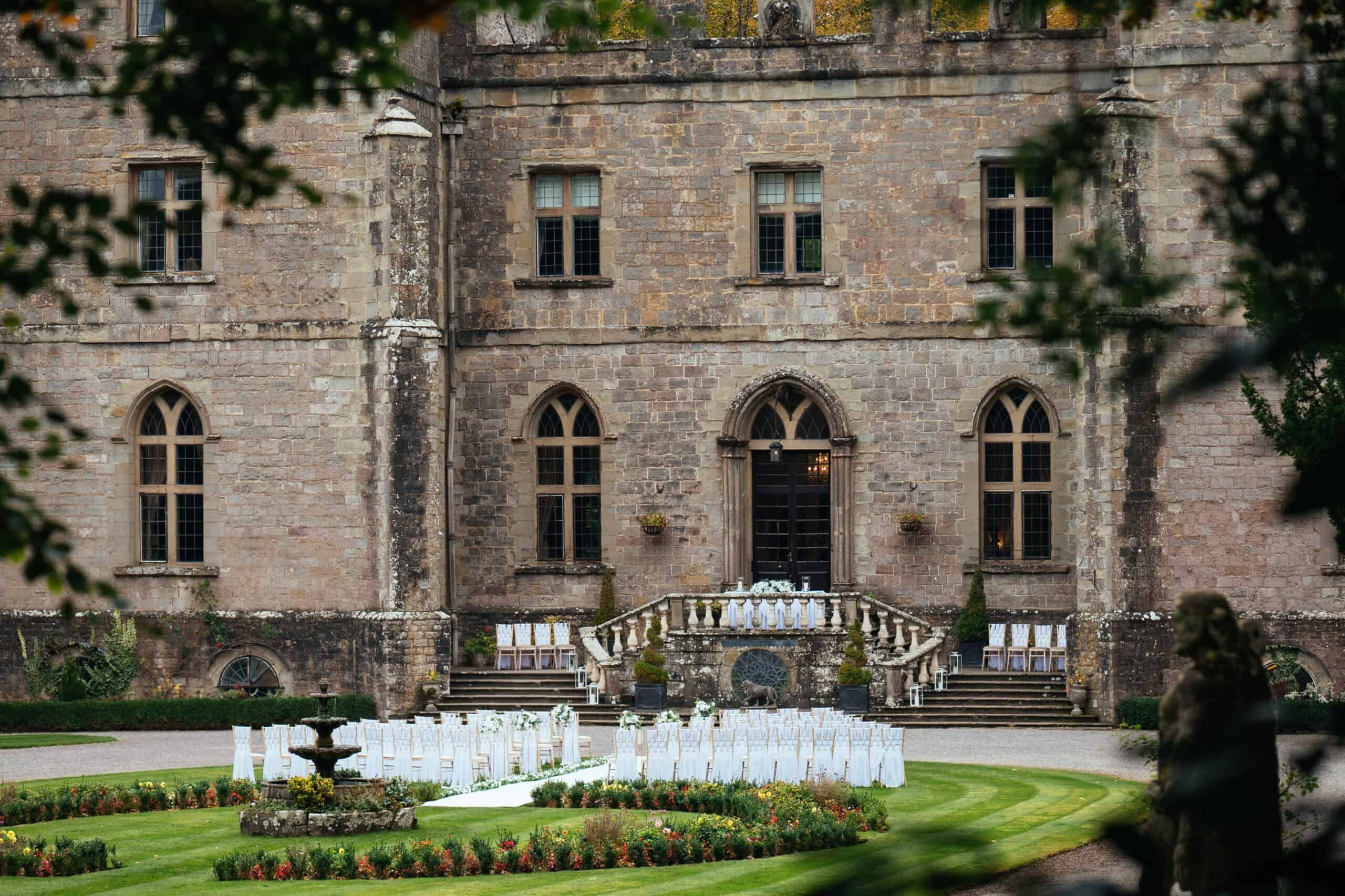 The rear elevation and balustraded terrace steps above a formal garden set with chairs for a ceremony, a fountain on the lawn, Clearwell Castle, Clearwell, England