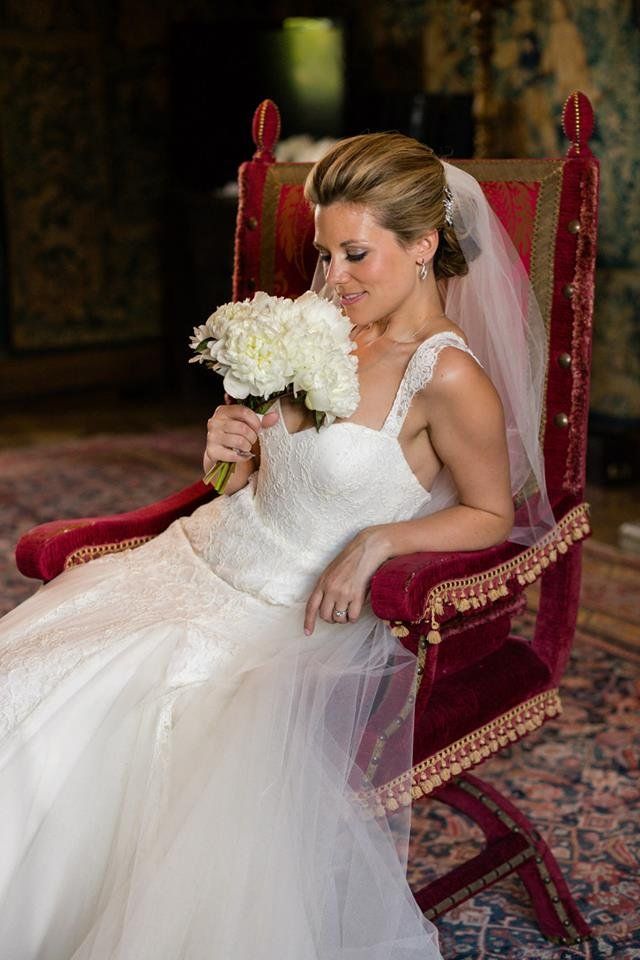 A bride seated in a carved red chair, holding a white bouquet