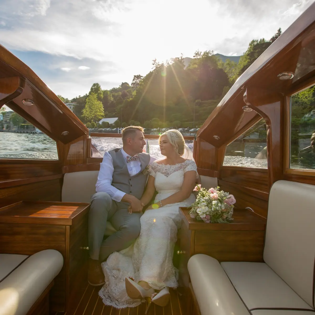 A couple seated in a varnished wooden boat on Lake Como, villas behind them