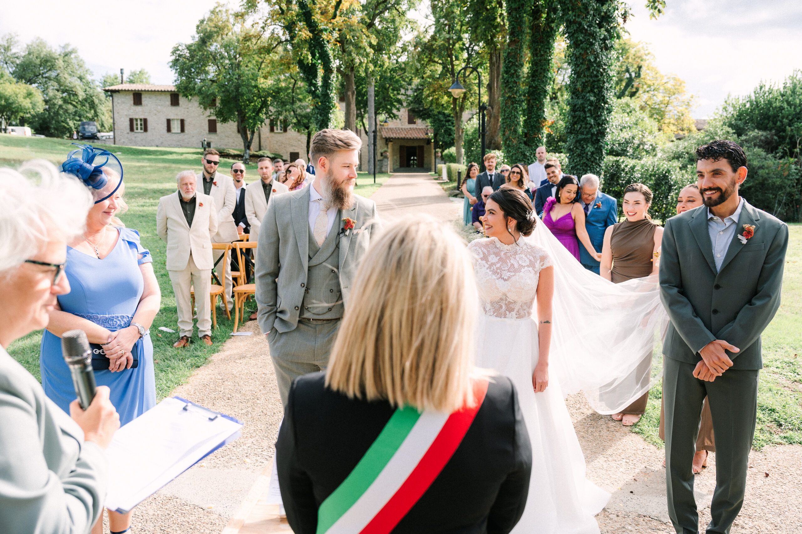 A civil ceremony outdoors, the officiant reading in the Italian tricolour sash