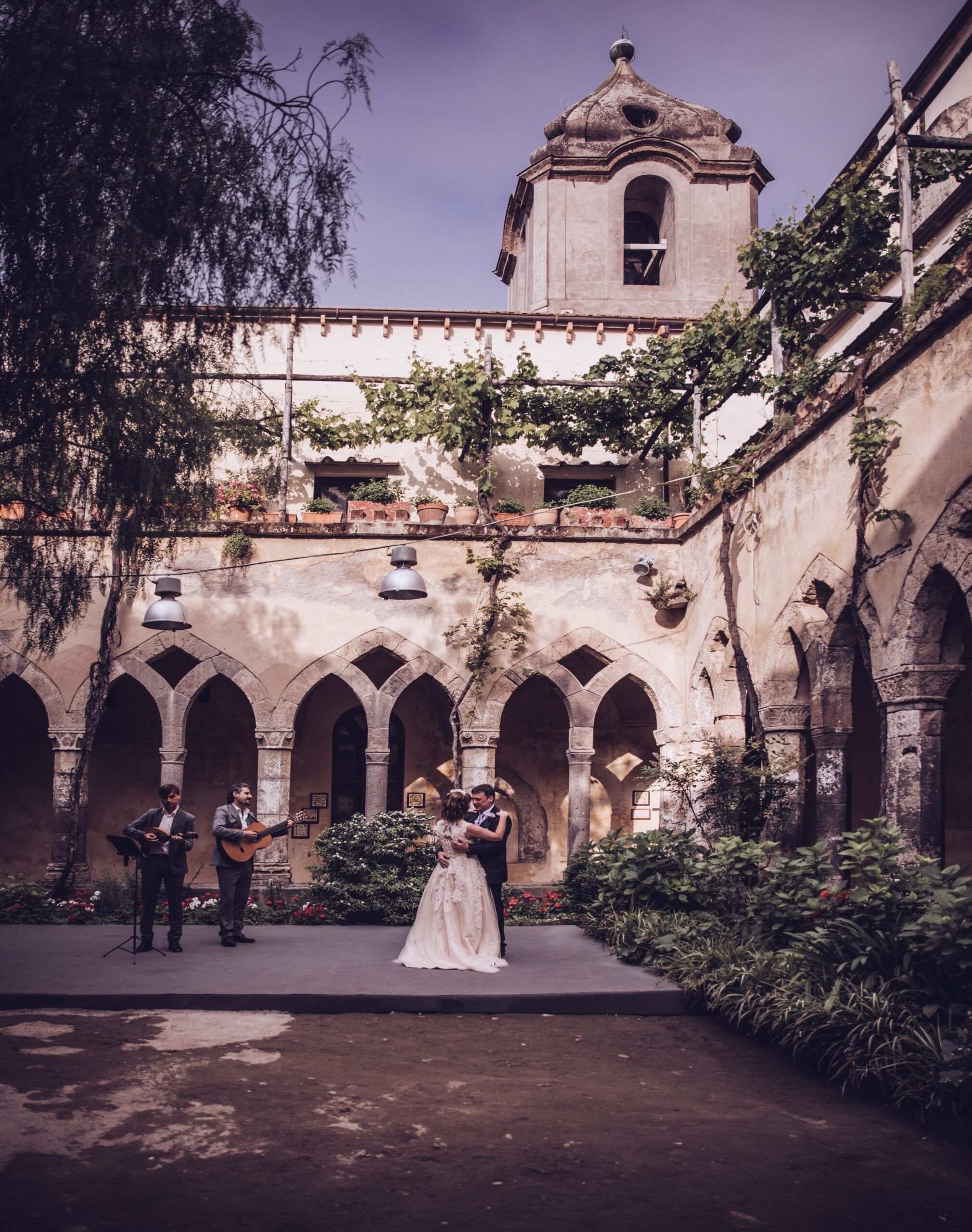 Newlyweds dancing in a stone cloister to two guitarists