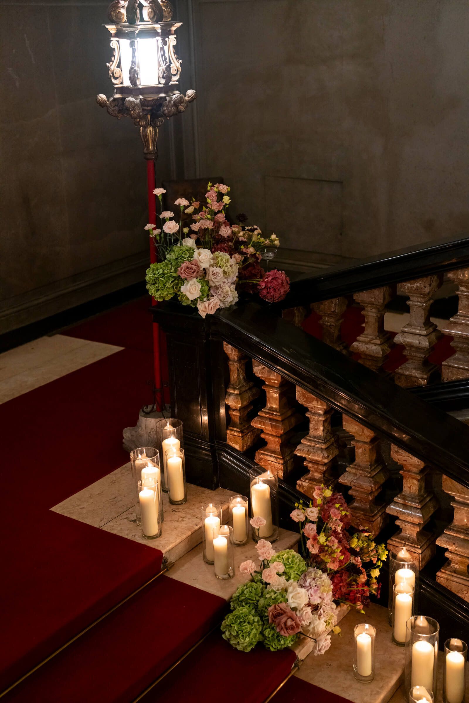 A close detail of the same staircase: blush and ivory roses gathered beside glass candle jars on a marble step
